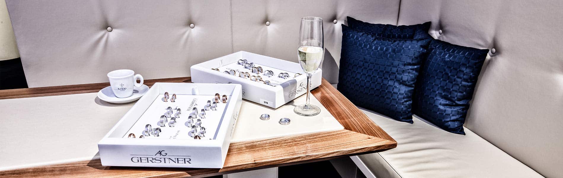 Sitzecke mit blauen Kissen Sektgläsern und Trauringen in der Trauringlounge des Juwelier Kopp