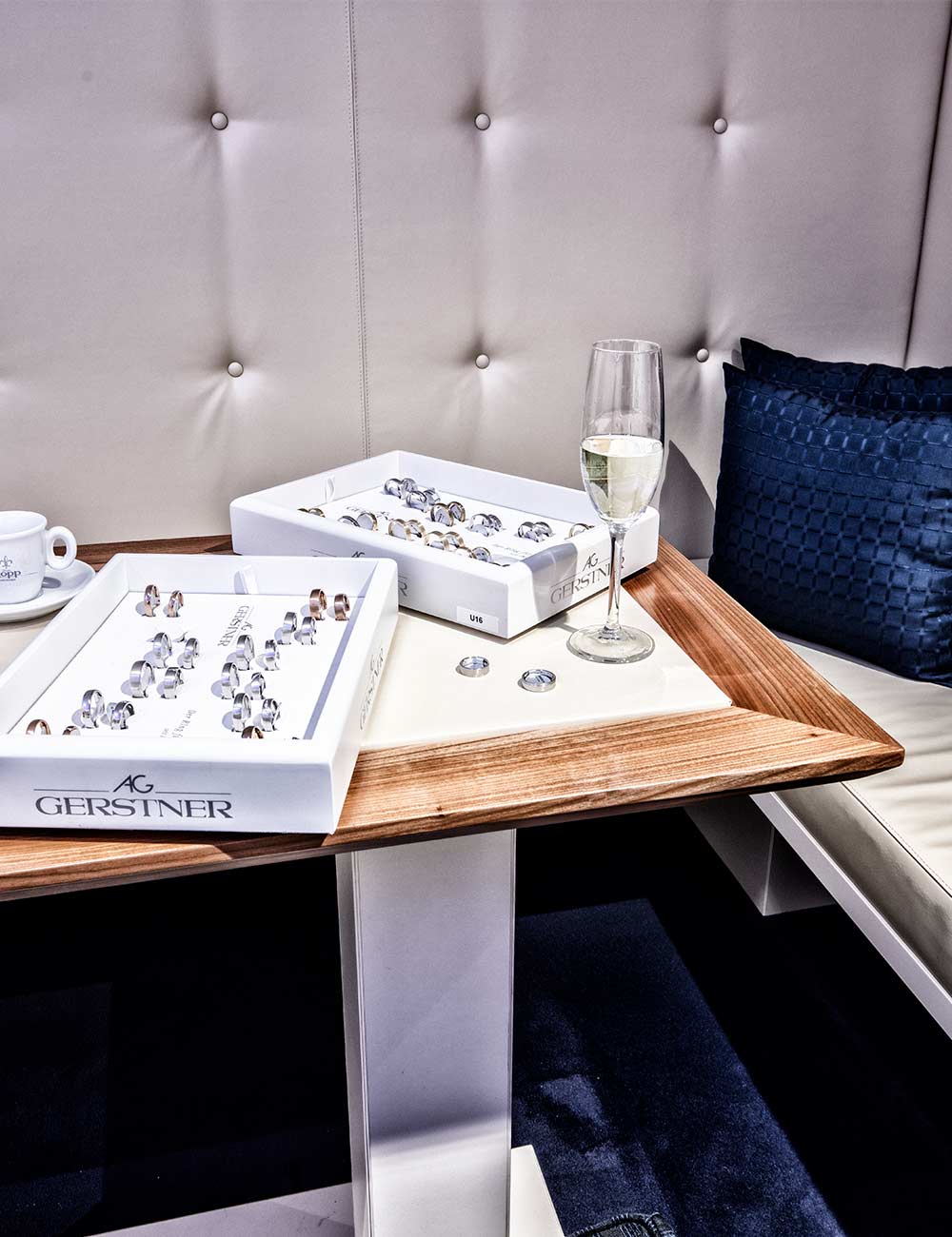 Sitzecke mit blauen Kissen Sektgläsern und Trauringen in der Juwelier Kopp Trauringlounge